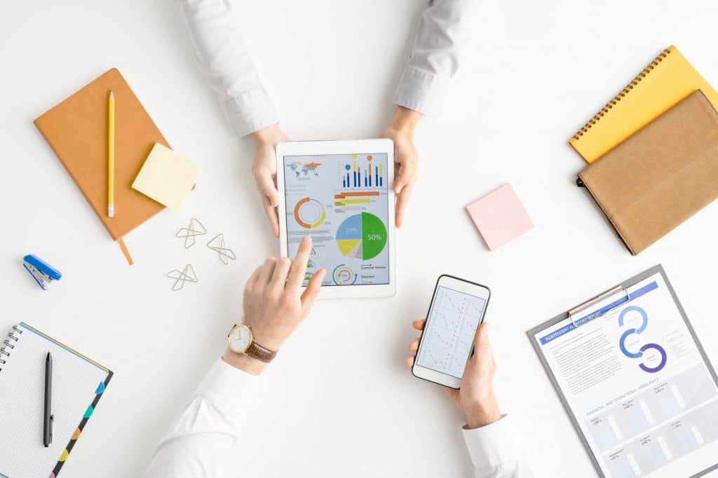 View of hands of analysts or brokers with gadgets discussing financial diagram